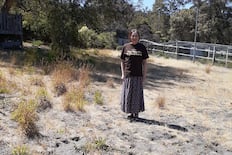 A woman wears a brown shirt that reads "Proud owner of The World's Ugliest Lawn" while standing in her yard, which she has not watered in years. Her lawn won a global contest encouraging people to send photos of lawns that they have kept dry to save water.